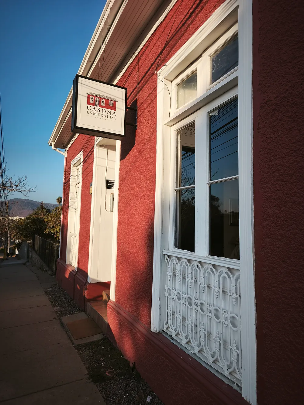 Fachada roja de Casona Esmeralda con gran ventana blanca y reja, a la luz del día