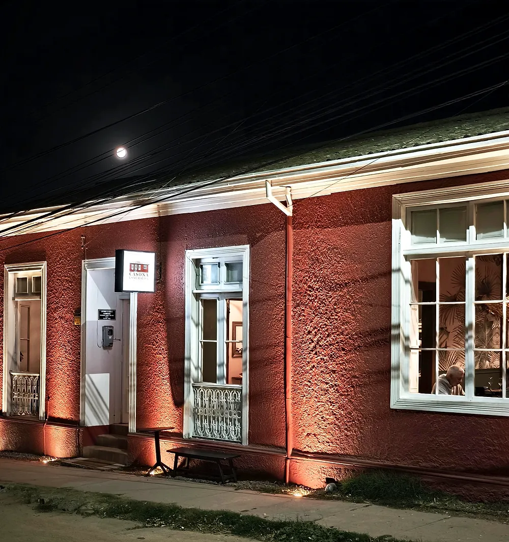 Fachada lateral de Casona Esmeralda de noche, con muros rojos iluminados