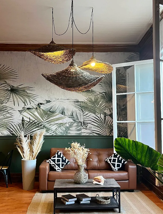 Sala de estar con sofá de cuero, mural de follaje y lámparas de fibra tejida