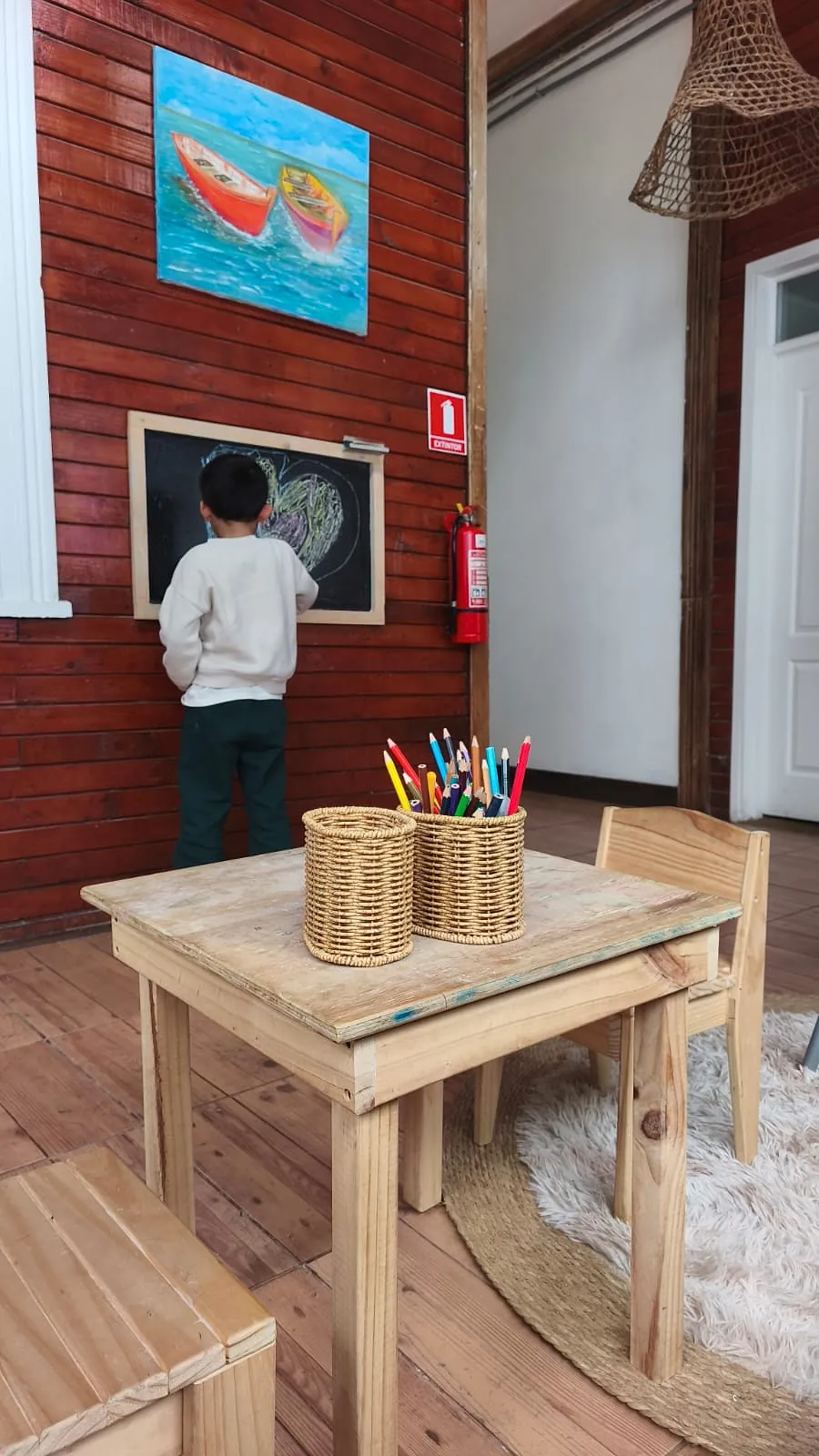 Zona infantil con mesa y sillas de madera, lápices de colores y una pizarra