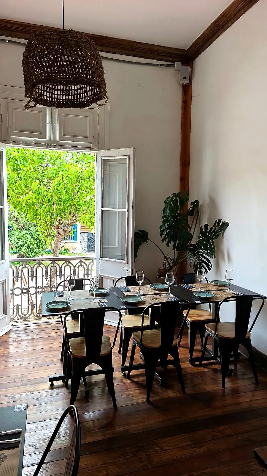 Salón con mesas y sillas junto a una puerta abierta al balcón y una lámpara de fibra