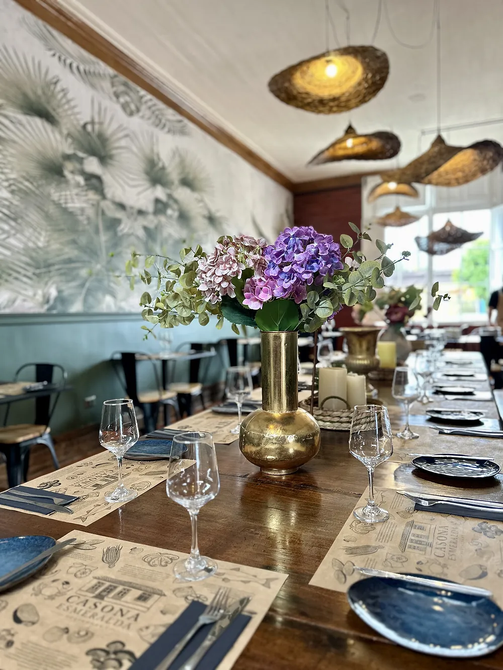 Mesa larga de madera con flores, copas y lámparas de fibra tejida en el salón