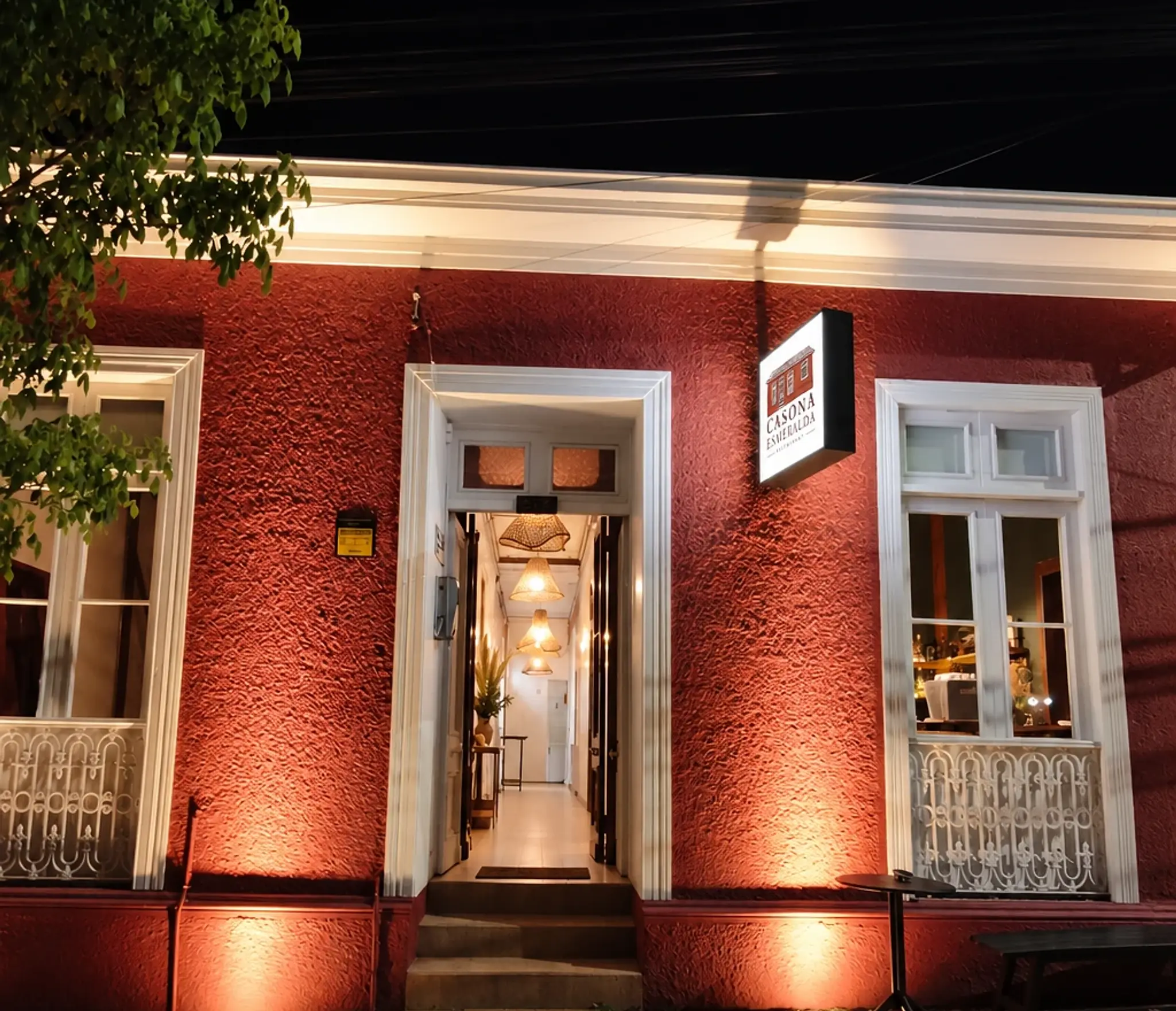 Fachada roja de Casona Esmeralda de noche, con la entrada iluminada y marcos blancos